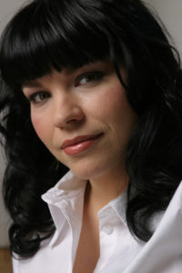 Ducky's face, with a slight smile and black hair in soft curls that reach her shoulders