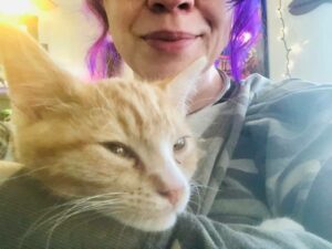 It a photo of my grinning face from my nose down, with a close up of Ragnar, my orange cat, resting his little head on my knee.